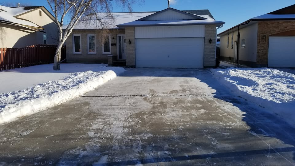 A residential driveway cleared of snow, with snow piled along the edges.