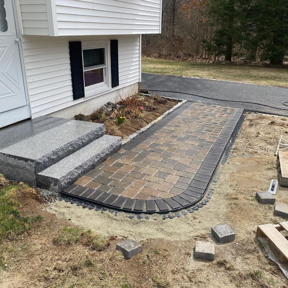 Newly installed curved paver walkway leading to granite steps at the entrance of a white house.